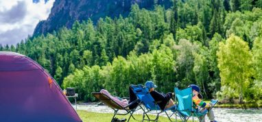 Family sitting outside tent by river and forest in Sweden
