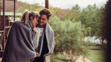 Holiday couple in hotel balcony wrapped in blanket