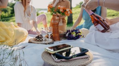 Digital Detox, time for disconnecting from electronic devices. Mobile phones on basket on picnic background. Group of young woman hanging out together on a picnic in nature at no phone zone